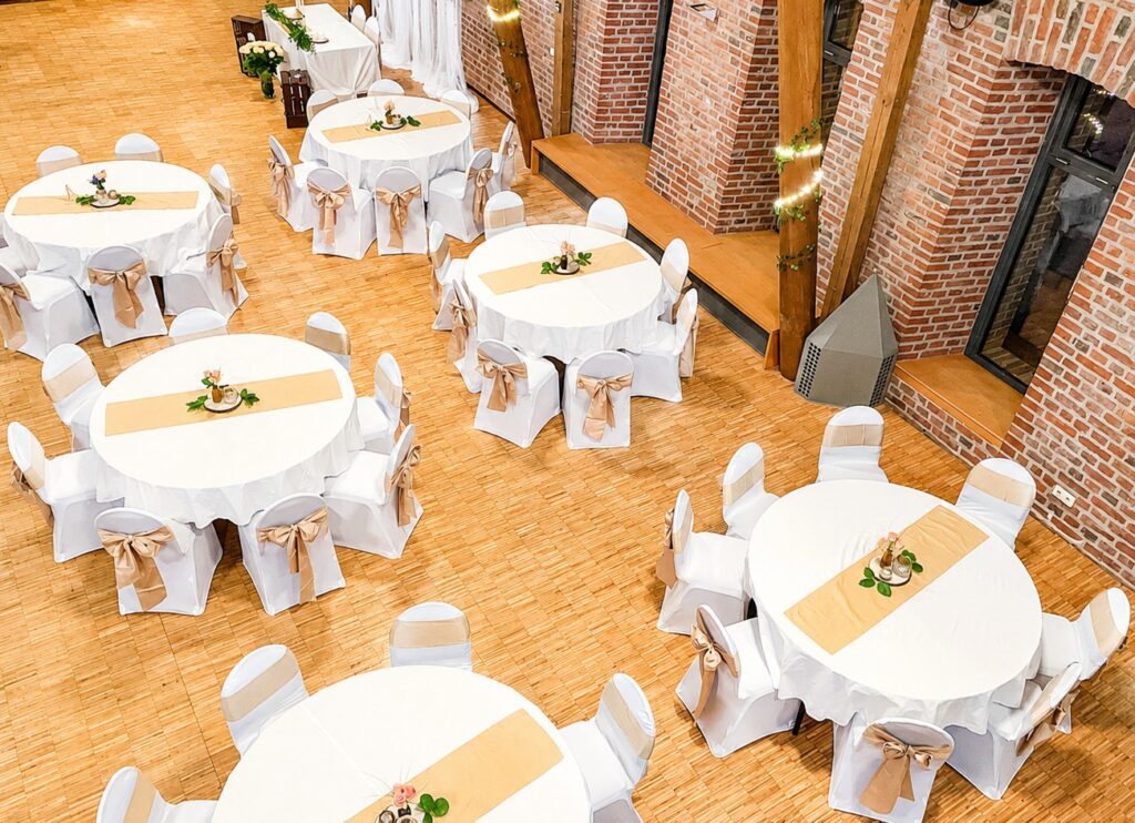 Weiße Stuhlhussen mit hellgoldenen Schleifen bei einer Hochzeit in der Zehntscheune Elsen in Grevenbroich.
