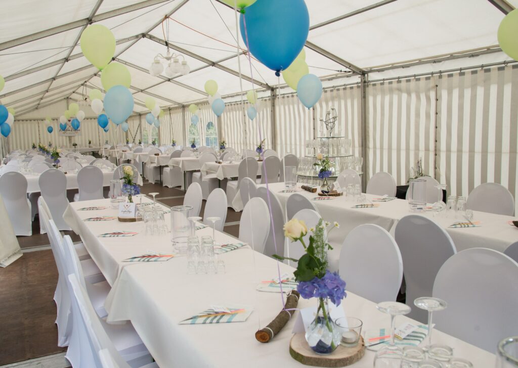 Hochzeit im Zelt mit weißen Stuhlhussen, gedeckten Tischen und festlicher Dekoration