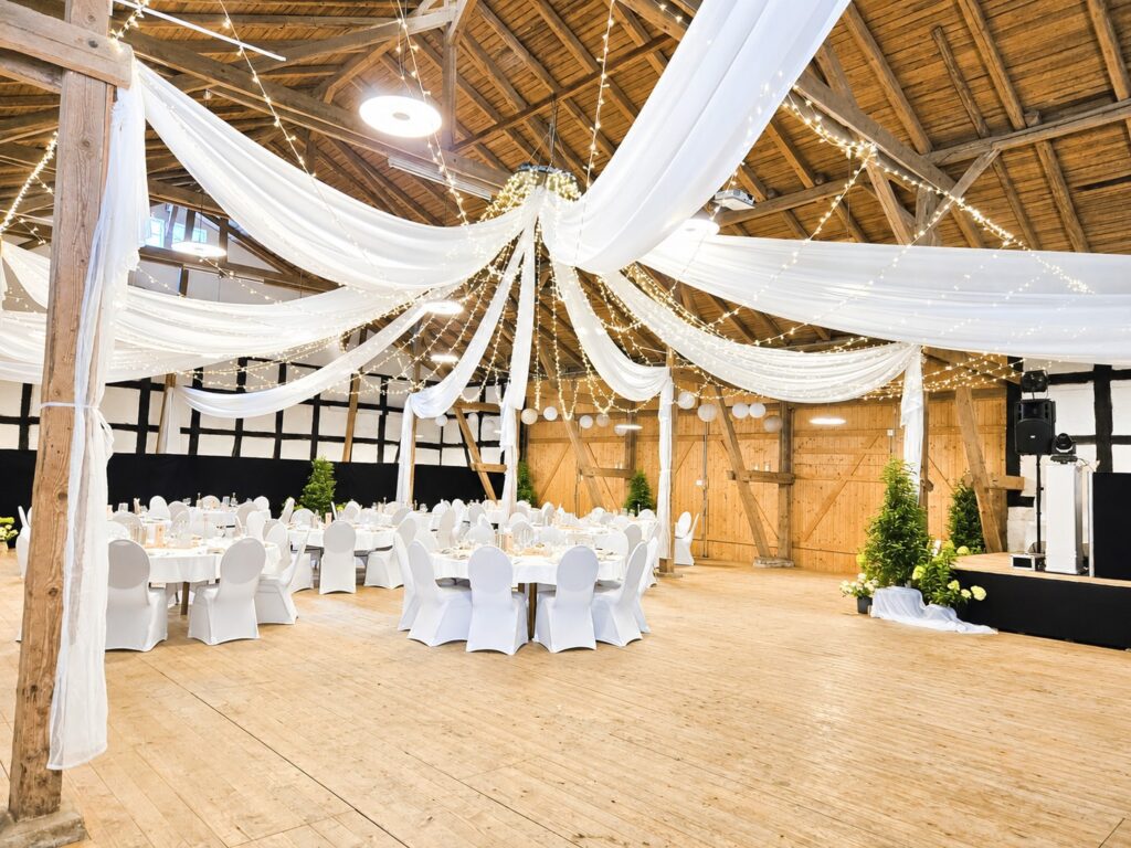 Weiße Stretch-Stuhlhussen und runde Tischdecken bei einer Hochzeit in der Eventlocation Zürns Hoff in Bötersen mit 120 Personen.
